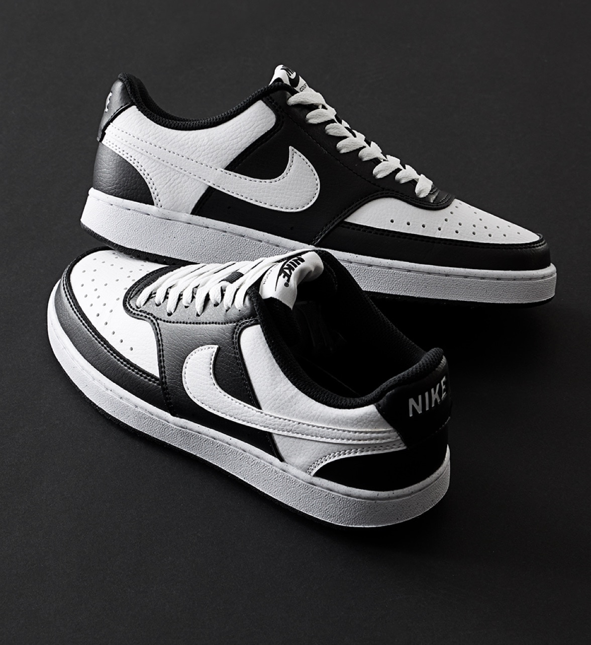 black and white panda nike court sneakers stacked on black background